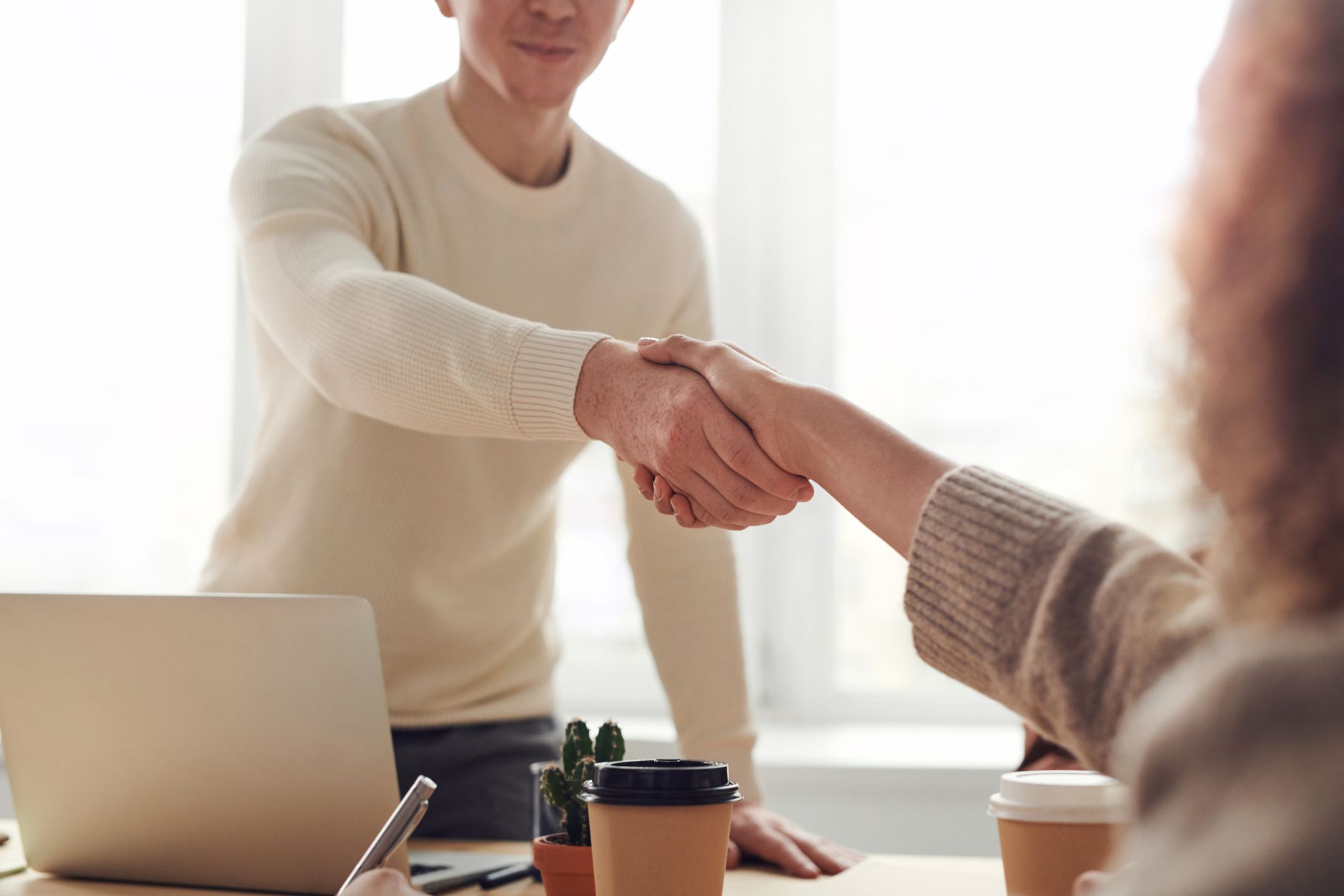 Two people shaking hands at a meeting table in a bright office